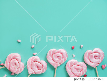 Pink lollipops in the shape of hearts with color sugar on a green background. Top view Pink lollipops in the shape of hearts with color sugar on a green background. Top view 116373606