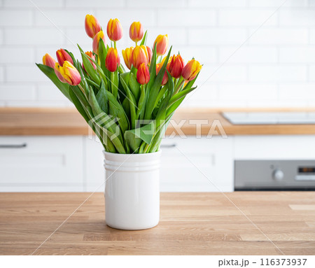 A beautiful bouquet of red and yellow tulips in a white vase on a wooden countertop A beautiful bouquet of red and yellow tulips in a white vase on a wooden countertop 116373937