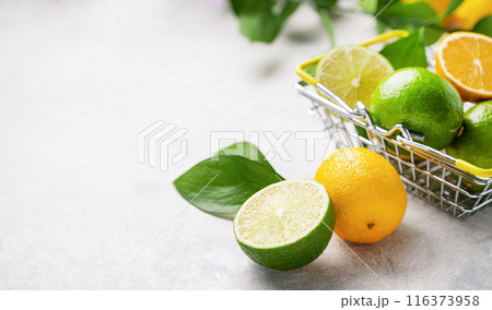 Fresh lemons and limes with leaves in a supermarket basket on a light textured background close up. 116373958