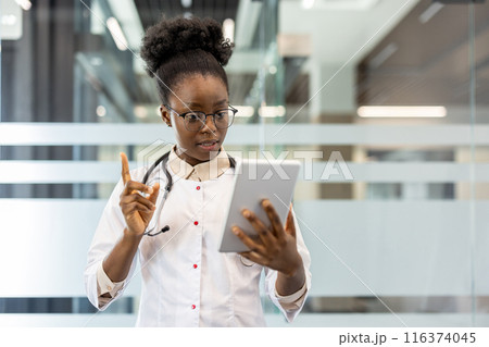 Female doctor wearing stethoscope using tablet for video call in modern office. Doctor making virtual consultation, communicating with patient. Professional healthcare worker using technology 116374045