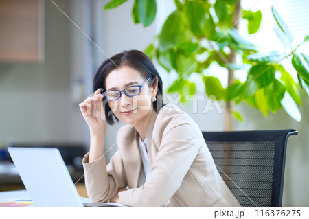 老眼鏡を掛けてオフィスのパソコンを見るミドル女性        116376275