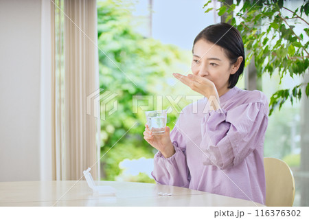 リビングで薬を飲む笑顔のミドル女性 116376302