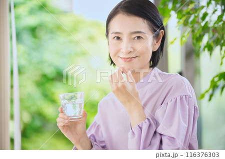 リビングで薬を飲む笑顔のミドル女性 116376303