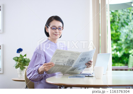 老眼鏡を掛けて英字新聞を読むミドル女性 116376304