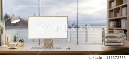 A computer with a white-screen mockup on a wooden table in a modern office with an ocean view. 116378753