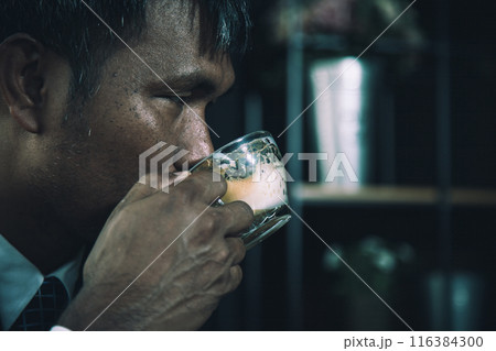 Close-up of businessman drinking coffee from glass cup, relaxation during work in dark office Close-up of businessman drinking coffee from glass cup, relaxation during work in dark office 116384300