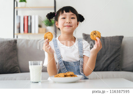 A young girl is sitting on a couch with a glass of milk and a plate of cookies 116387595