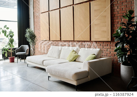 Roomy waiting zone in office made in loft style, zone equipped with ficuses in clay pots and white suede sofa and light suede armchair 116387924