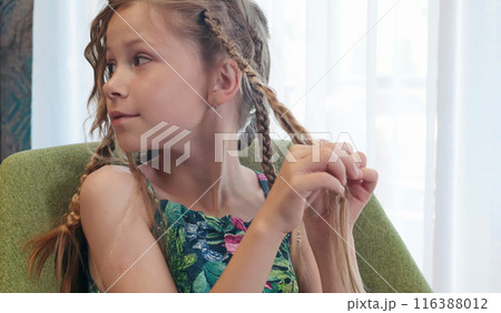 Teenage girl unbraiding pigtails in room on chair. Beauty and hair care.  116388012
