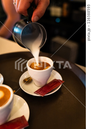 Waiter's hand pouring milk with the pitcher into a coffee cup. Vertical 116388593
