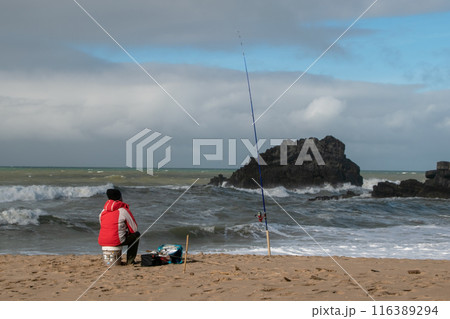 Fisherman on the sandy beach of the Atlantic Ocean in winter, man alone by the sea, beautiful cloudscape, dramatic landscape, gloomy seascape, big sea waves 116389294