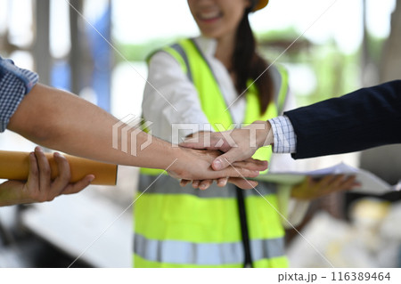 Construction workers stacking hands to motivate and working as teamwork on construction site. Construction workers stacking hands to motivate and working as teamwork on construction site. 116389464
