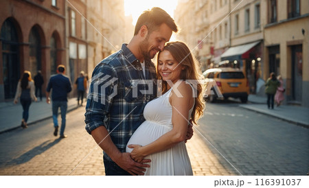 A couple, the man in a plaid shirt and the woman in a white dress, standing on a city street, holding her pregnant belly and smiling warmly. 116391037