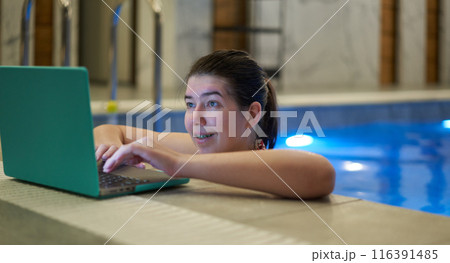 Woman Typing on Laptop with Smile in Swimming Pool 116391485