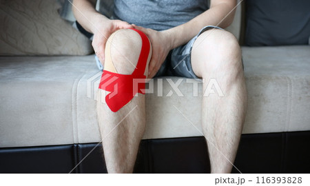Male hands holding sored knee sitting on couch at home Male hands holding sored knee sitting on couch at home 116393828