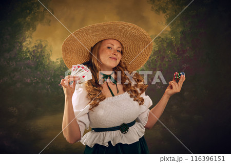 Woman in historical attire, wearing a large straw hat, white blouse, and green skirt, smiling and holding playing cards and stack of poker chips, against vintage background. 116396151