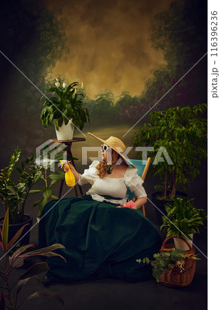 Gardening. Elegant woman in skirt, blouse, sunglasses and hat, sitting on chair in garden and spraying plants with water, set against vintage background 116396236