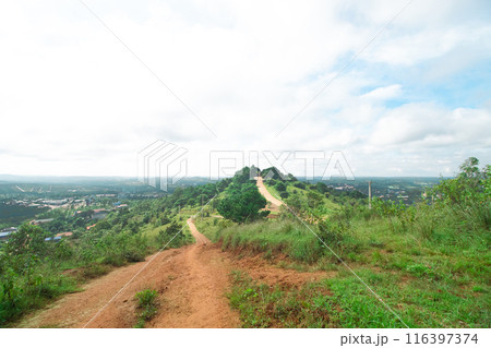 A dirt path winds up a green hill, flanked by trees and greenery under a cloudy sky, with a view of the horizon. Mondulkiri, Cambodia A dirt path winds up a green hill, flanked by trees and greenery under a cloudy sky, with a view of the horizon. Mondulkiri, Cambodia 116397374