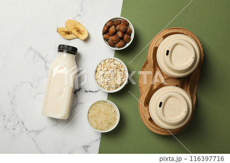 Bottle of alternative milk, herbal ingredients and paper cups on white and green background, top view Bottle of alternative milk, herbal ingredients and paper cups on white and green background, top view 116397716