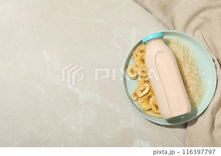 Bottle with milk on plate with rice and sliced bananas, towel on beige background, space for text Bottle with milk on plate with rice and sliced bananas, towel on beige background, space for text 116397797
