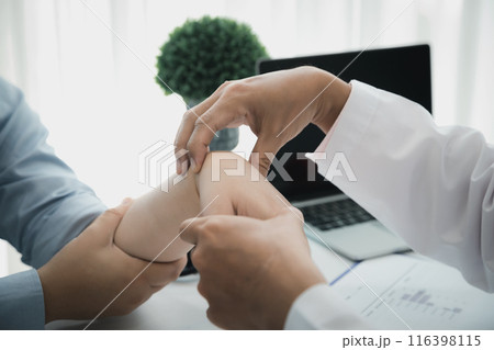 Orthopaedic doctor doing physical examination patient with wrist pain at the clinic. Physical therapist checks the patient wrist by pressing the wrist bone. 116398115
