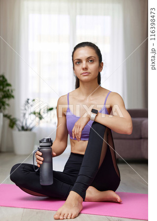 caucasian woman drinking water sitting on pink exercise mat at home caucasian woman drinking water sitting on pink exercise mat at home 116398473
