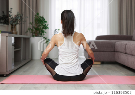 Back view of sporty woman practicing yoga and meditation sitting in lotus pose on pink yoga mat at home 116398503