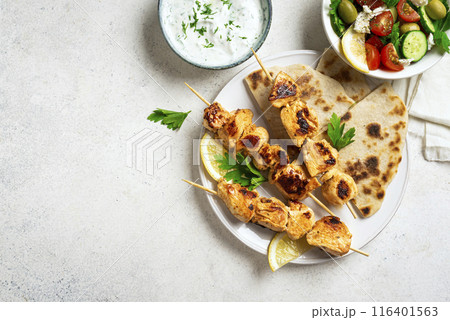 Chicken souvlaki kebabs with flatbread and greek salad 116401563