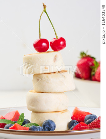 A stack of four cheesecakes on a plate with berries, blueberries, strawberries and cherries. 116403549