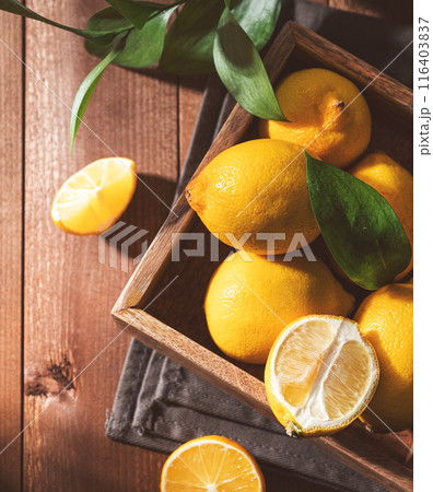 Fresh lemons with leaves in a wooden box on a dark board background close up.  116403837
