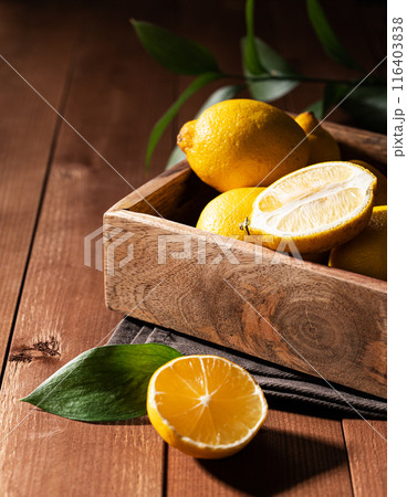 Fresh lemons with leaves in a wooden box on a dark board background close up.  116403838