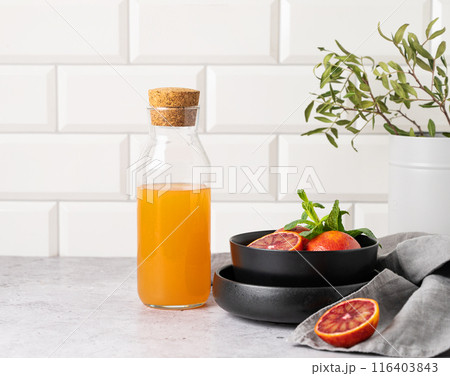 Freshly squeezed orange juice in a bottle on the kitchen table with fresh red oranges on plate.  116403843