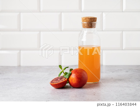 Freshly squeezed orange juice in a bottle on the kitchen table with fresh red oranges.  116403844