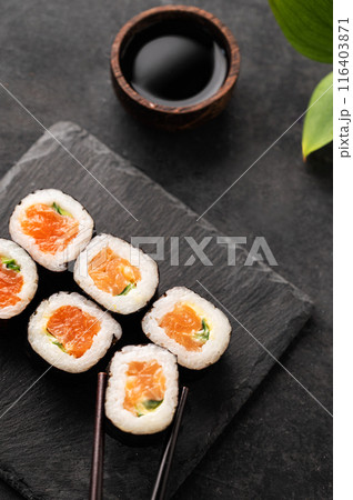 The concept of sushi maki with salmon, cucumber and nori on black slate boards with soy sauce.  116403871