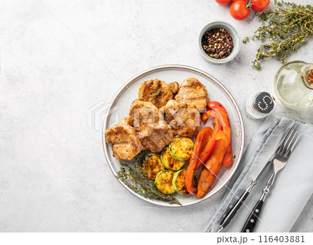 Grilled pork dish with fresh vegetables pepper and zucchini  in a plate on a blue background Grilled pork dish with fresh vegetables pepper and zucchini  in a plate on a blue background 116403881