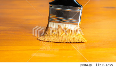 Painting table with brown enamel, brush in hand close-up, painting wood furniture process with brownish dye 116404259