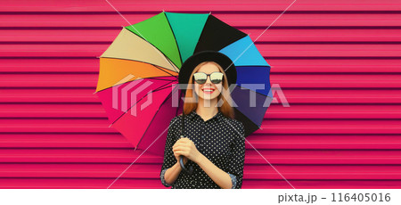 Portrait stylish happy smiling young woman holding colorful umbrella in glasses on pink background 116405016