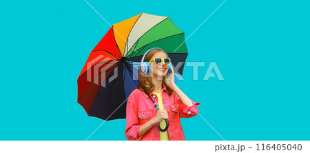 Happy smiling young woman with colorful umbrella listening to music in headphones on blue background Happy smiling young woman with colorful umbrella listening to music in headphones on blue background 116405040