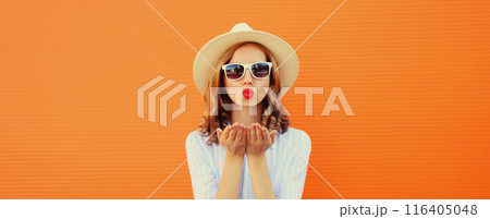 Portrait of beautiful stylish young woman blowing a kiss in summer hat, glasses on orange background 116405048