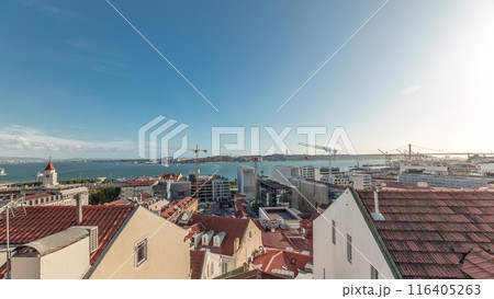 Panorama showing red roofs timelapse and 25 de Abril Bridge, Iconic suspension bridge over Tagus River in Lisbon, Portugal. 116405263