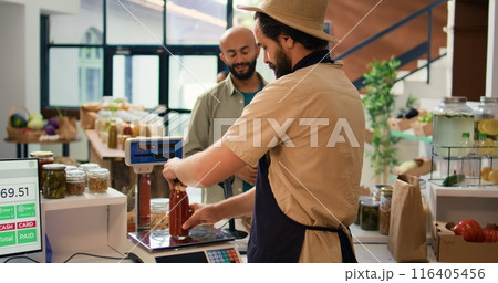 Man checking weight of produce using modern market scale and selling fresh items to customer. Local grocery store vendor weighting potatoes and pasta in reusable container. Handheld shot. 116405456