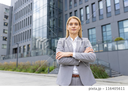 Confident businesswoman standing with arms crossed in front of modern office building. Professional attire, leadership, success. Urban background. Concept of career, business 116405611