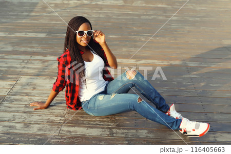 Modern happy young african woman smiles sitting on the floor with dreadlocks, black girl in the city Modern happy young african woman smiles sitting on the floor with dreadlocks, black girl in the city 116405663