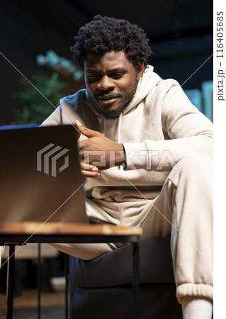 BIPOC remote employee sitting at home on couch late at night in front of laptop, overthinking problems. Man struggling to finish job tasks before deadline, trying to come up with solutions 116405685