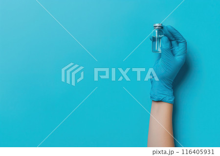 Female doctor's hand in blue medical gloves holds a bottle of vaccine on a blue background 116405931