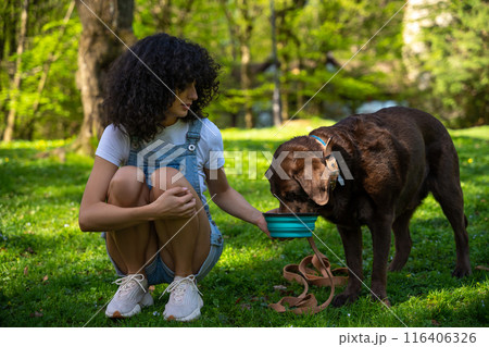 Dog owner giving water to her pet in the park 116406326