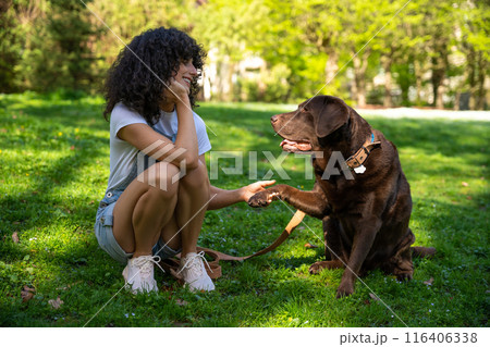 Curly-haired young woman playing with her dog in the park Curly-haired young woman playing with her dog in the park 116406338
