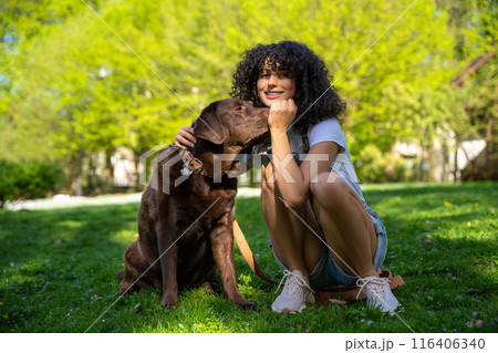 Curly-haired young woman playing with her dog in the park Curly-haired young woman playing with her dog in the park 116406340