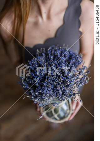 A serene woman holding a lavender bouquet in a rustic vase, embodying simplicity and natural beauty 116406459