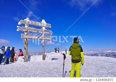 真冬の快晴の日本北海道のルスツスキー場、イーストエリアのイゾラ山頂の標識と羊蹄山とスキーヤーやスノー 116406855